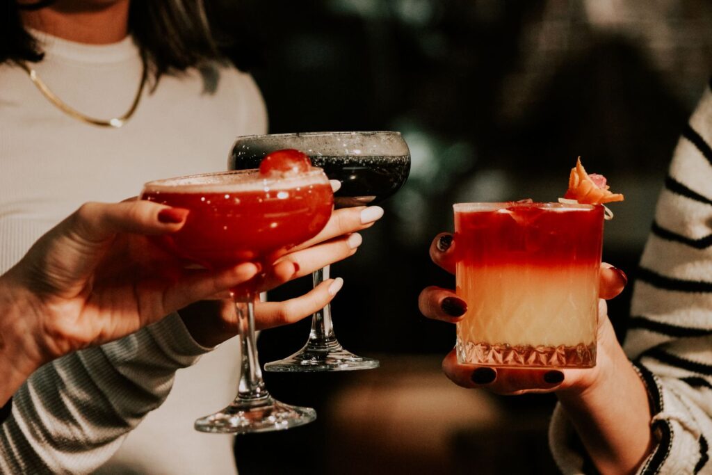 Three women clinking colorful cocktails at a festive bar