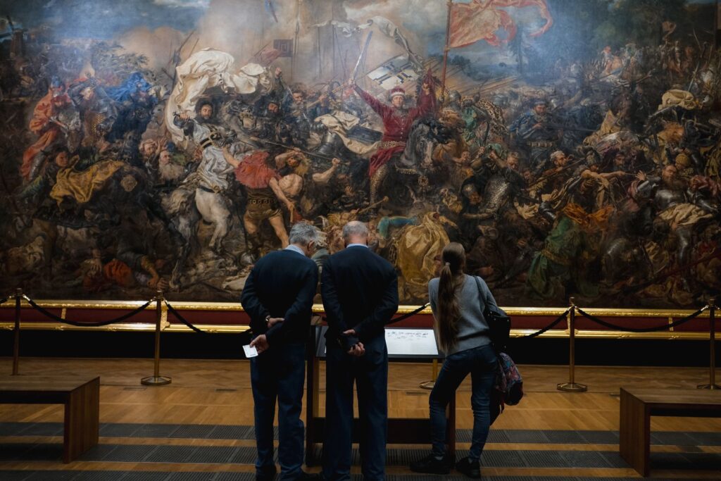 Visitors studying a large painting in a museum gallery