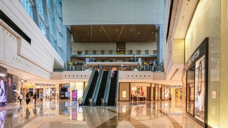 Shopping mall interior with escalators and storefronts